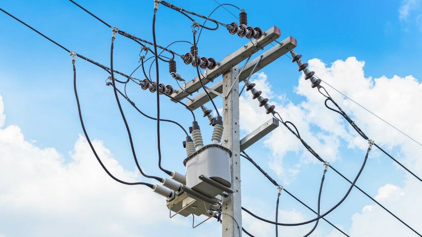 Poste de distribución eléctrica con transformador contra un cielo azul